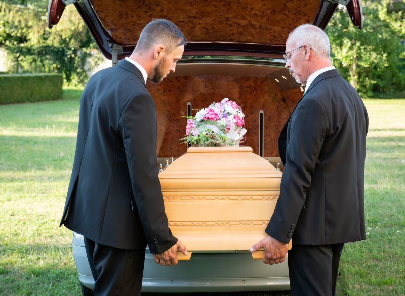 Trauerbegleiter laden Sarg in ein Bestattungswagen